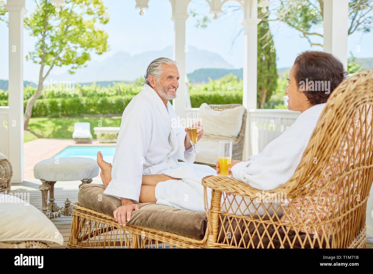 Mature couple in bathrobes relaxing, drinking mimosas in resort gazebo Stock Photo