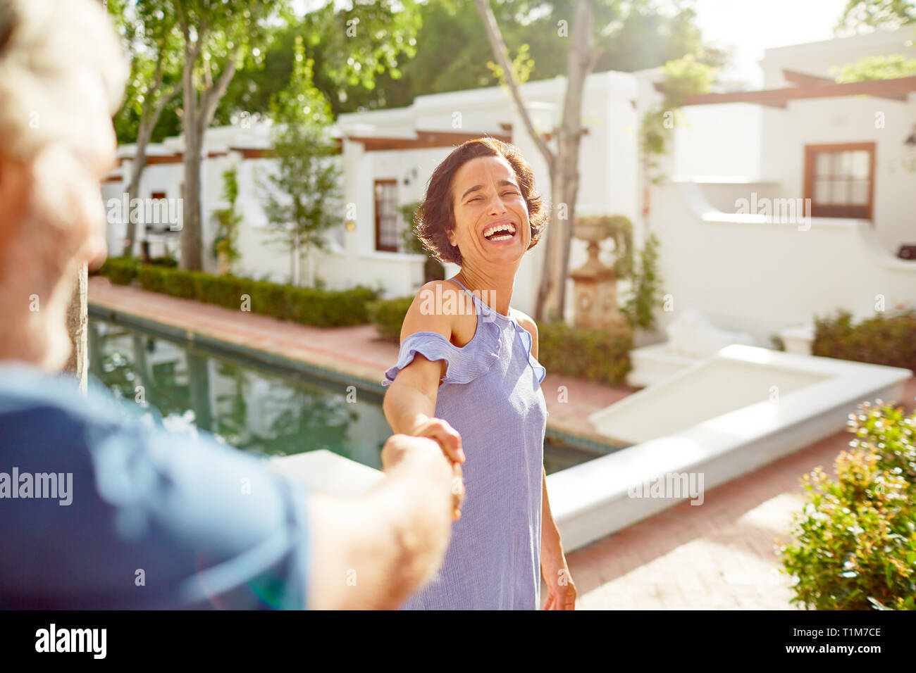 Happy, carefree mature couple holding hands at sunny resort poolside Stock Photo