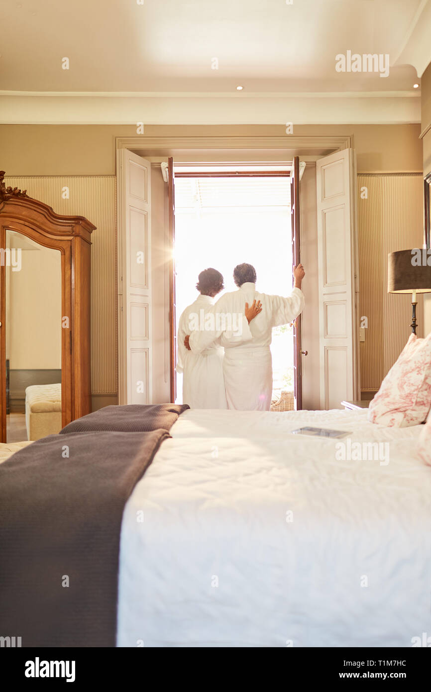 Affectionate couple in spa bathrobes standing at hotel balcony doorway Stock Photo