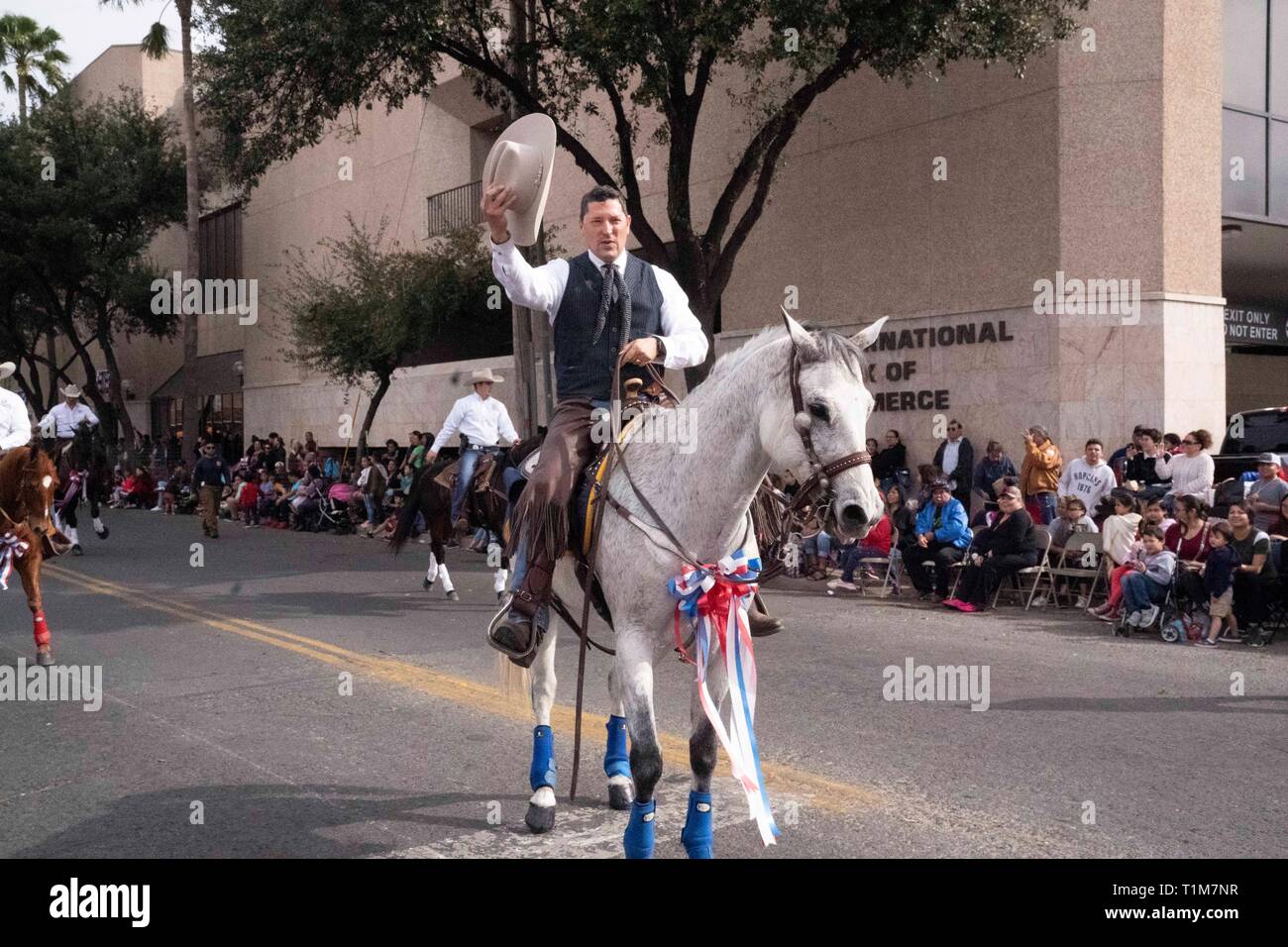 A man dressed in traditional charreada clothing waves his hat while riding a horse in the annual Washington's Birthday Celebration parade in Laredo TX Stock Photo