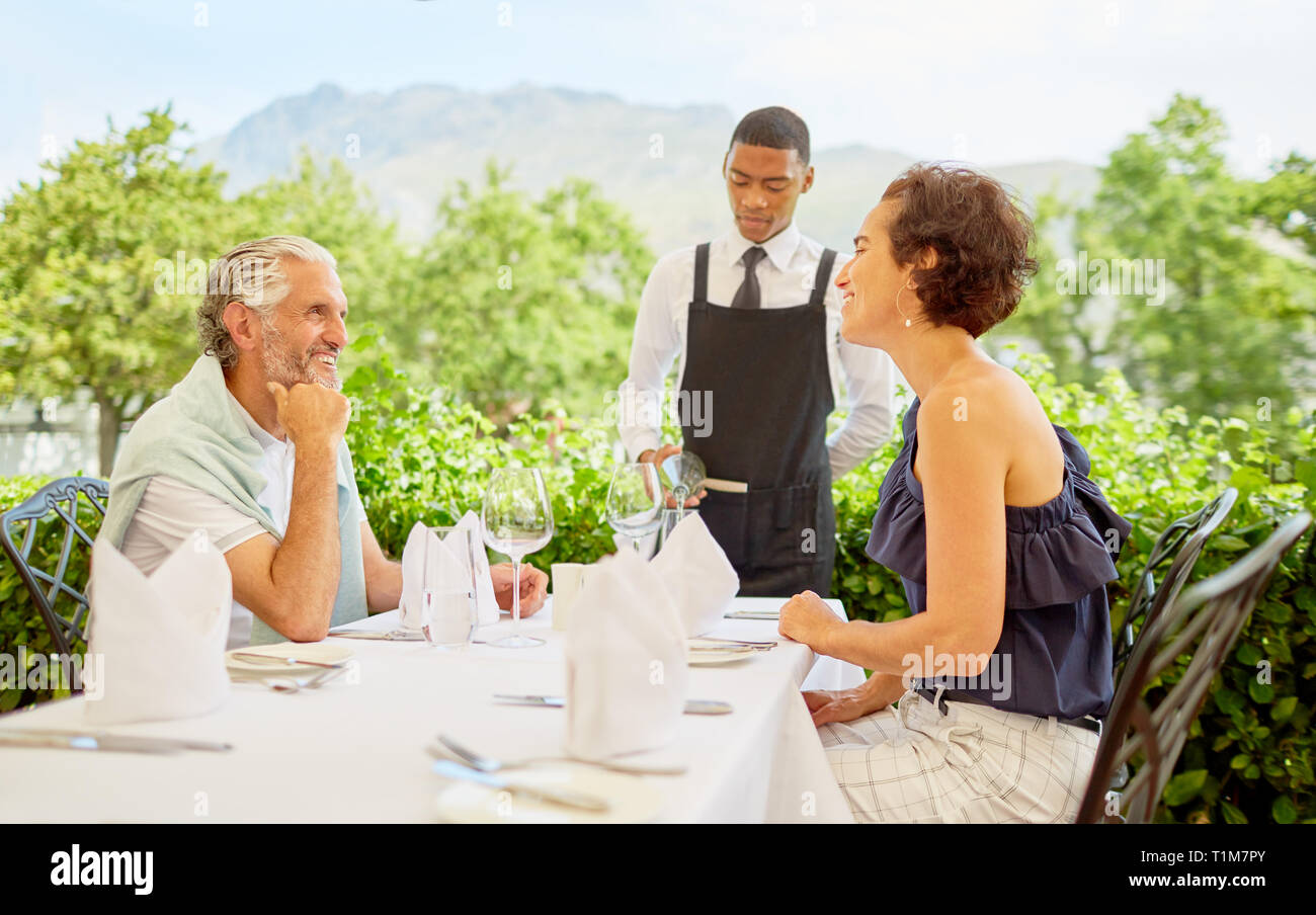 Wine steward pouring wine for mature couple dining at patio table Stock Photo