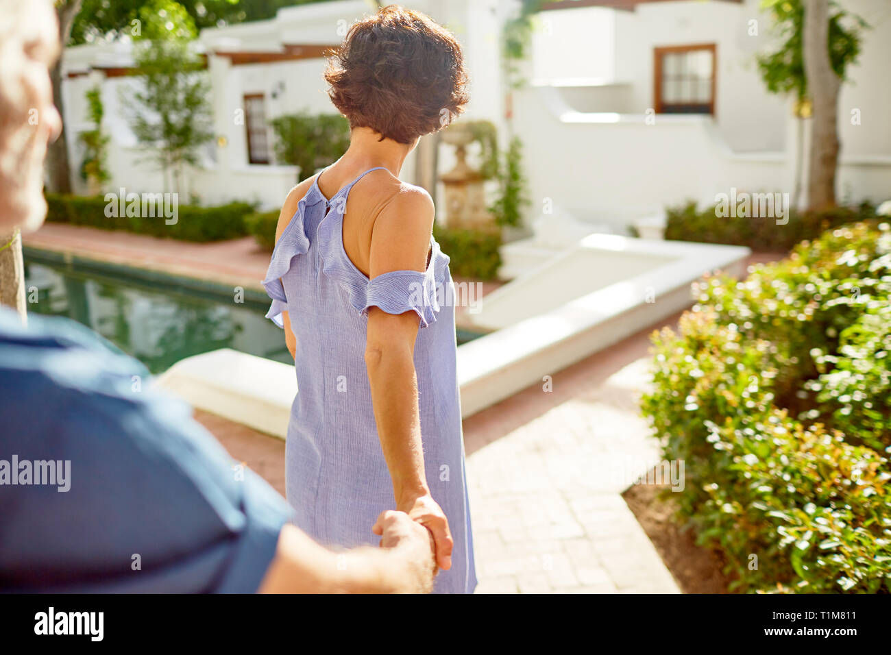 Couple holding hands, walking at sunny poolside Stock Photo