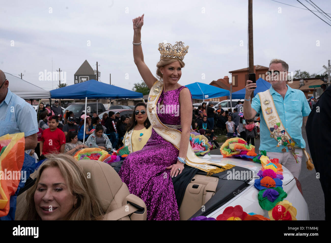 Young woman wearing crown sits on back of convertible car and waves to
