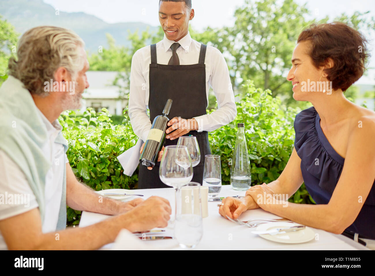 Wine steward showing wine bottle to mature couple dining on patio Stock Photo