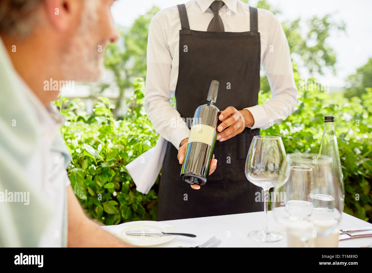 Wine steward showing wine bottle to man dining on patio Stock Photo