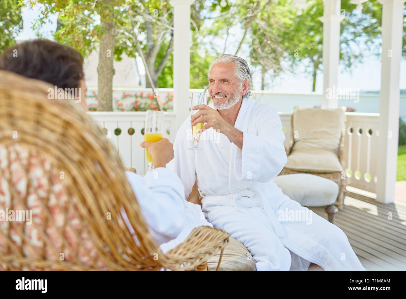 Mature couple in spa bathrobes drinking mimosas in resort gazebo Stock Photo