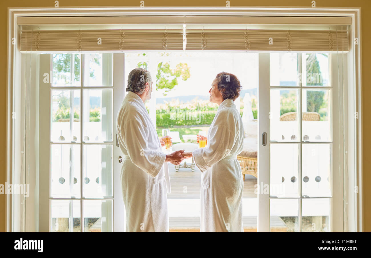 Mature couple in spa bathrobes drinking mimosas at hotel patio door Stock Photo