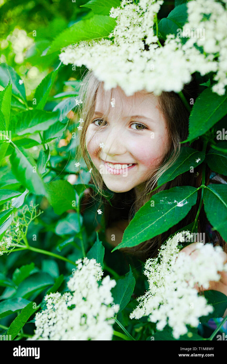 Portrait smiling girl hiding in blooming bush Stock Photo