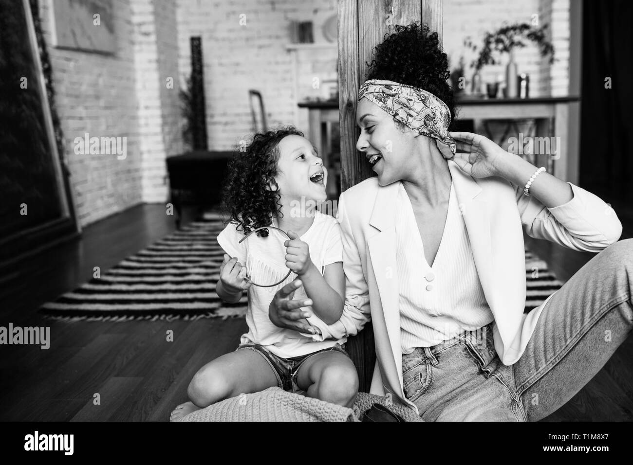 A cute curly girl and her mother are sitting in the living room on the floor. Stock Photo