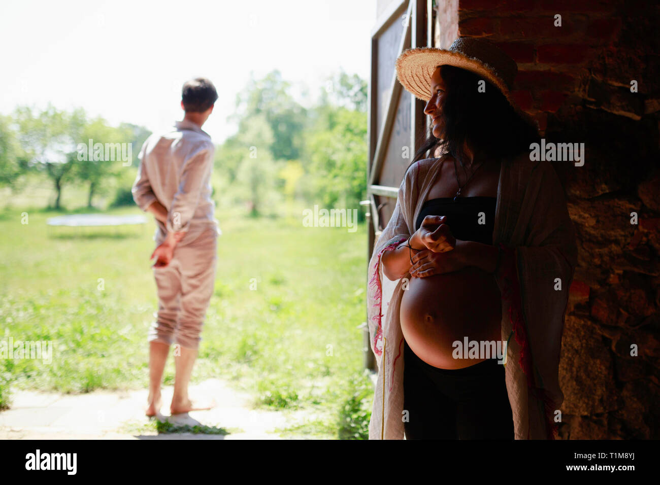Pregnant woman watching man in barn doorway Stock Photo