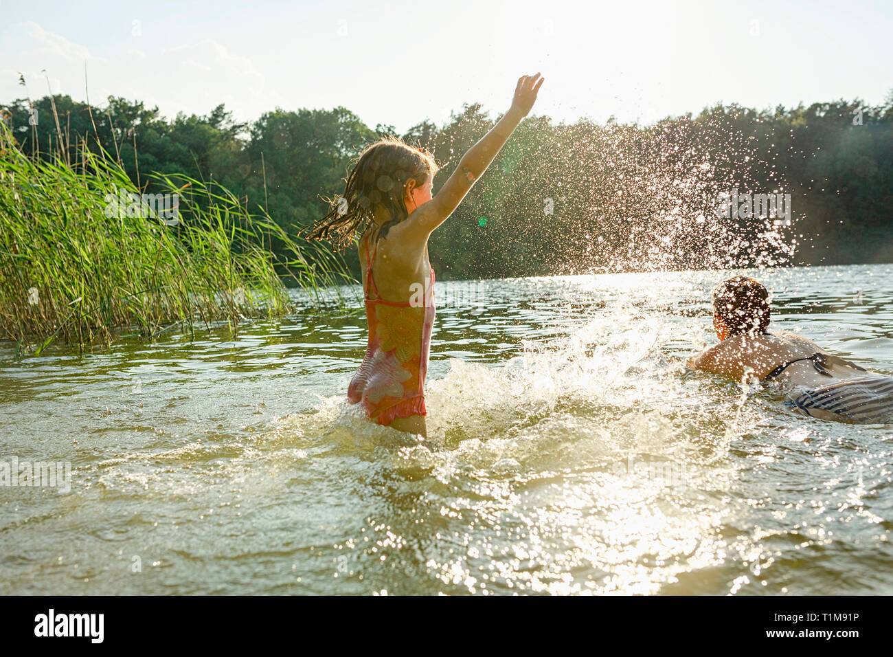 Playful girl splashing and woman swimming in sunny summer lake Stock Photo
