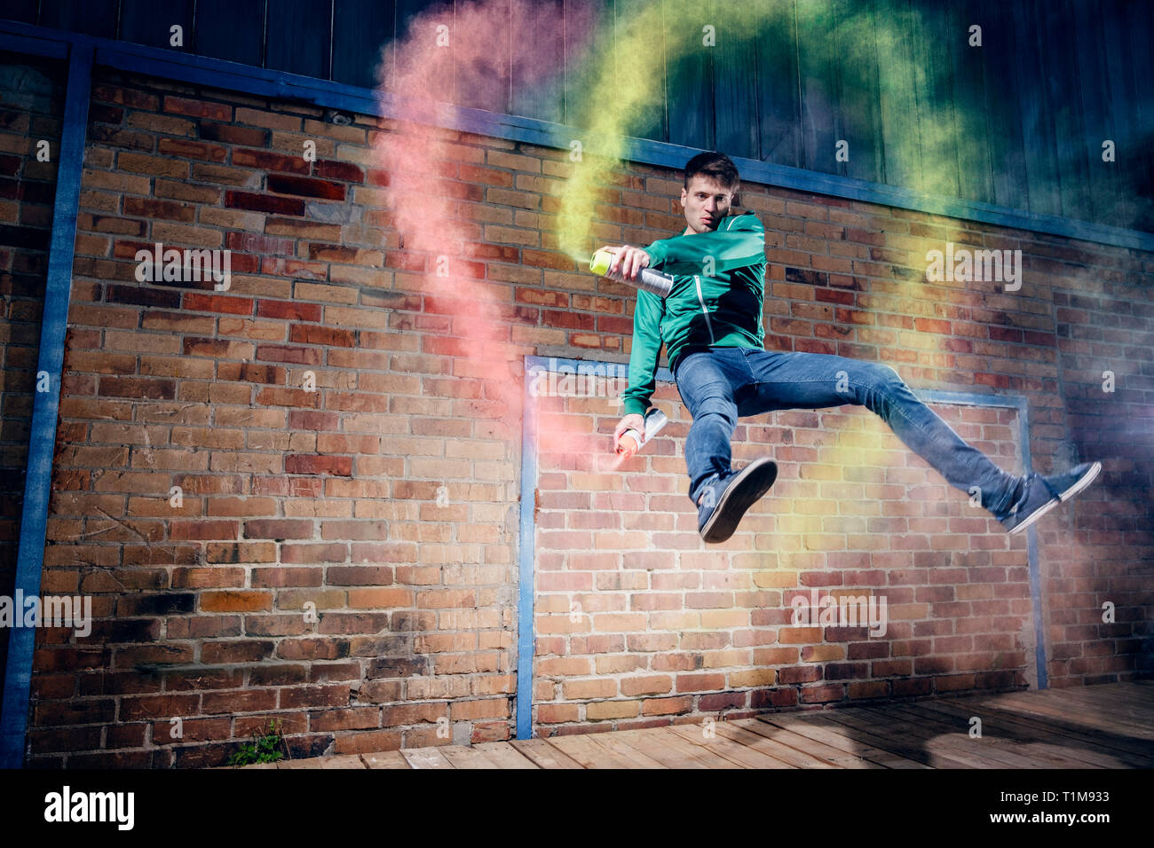 Portrait male modern dancer performing with spray paint against brick wall Stock Photo