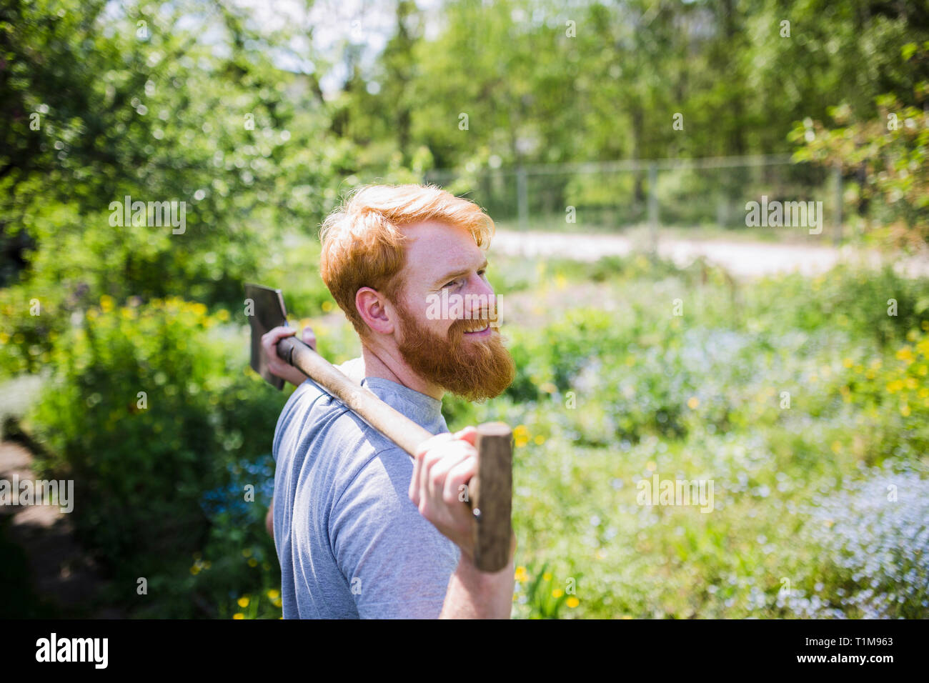 Smiling man with beard holding shovel in sunny garden Stock Photo