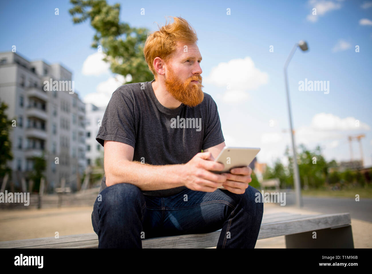 Hipster man with beard using digital tablet on urban bench Stock Photo