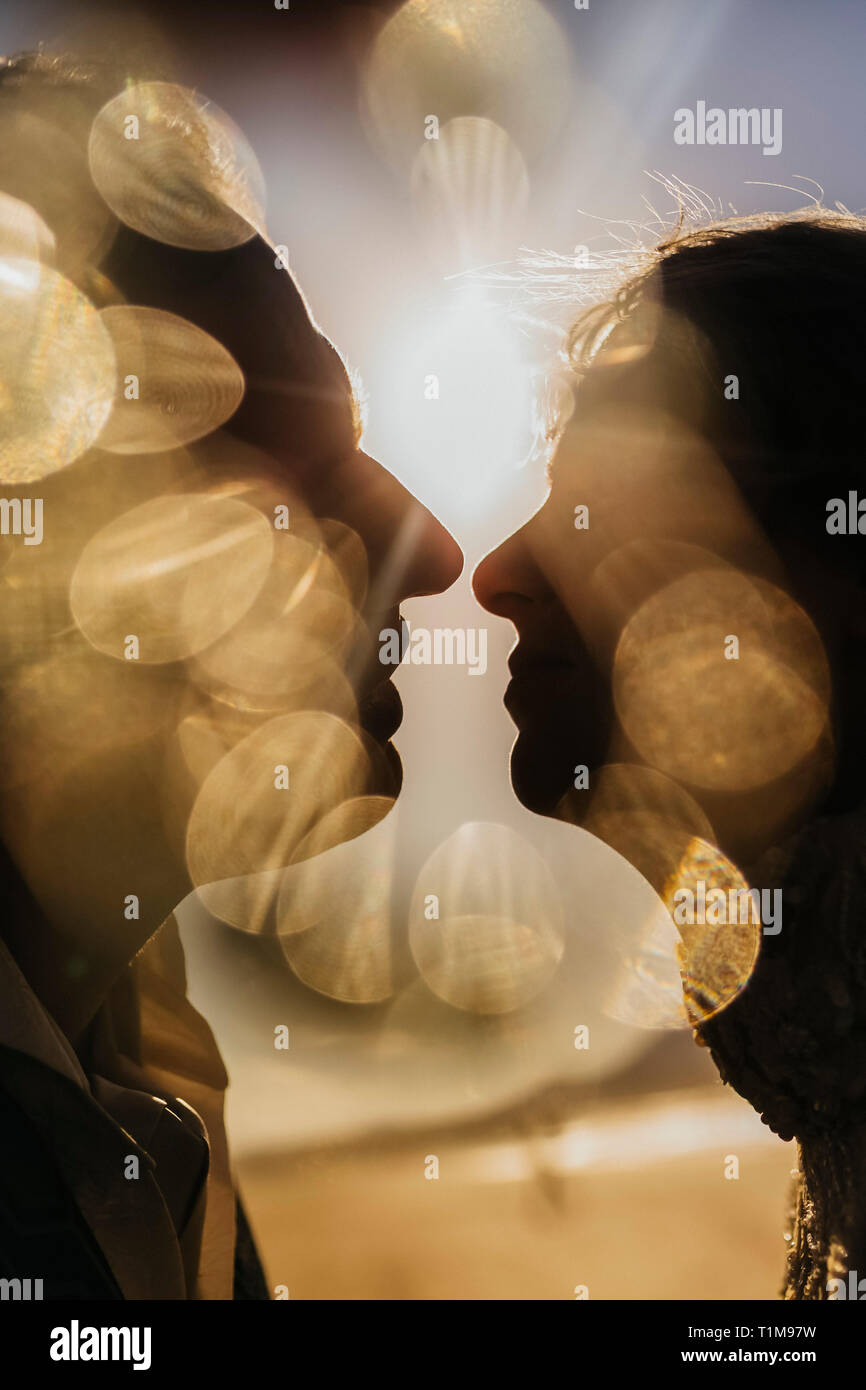 Golden light illuminating silhouetted profile of couple kissing Stock Photo