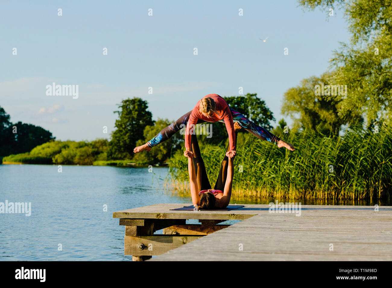 Women practicing acro yoga on sunny lakeside dock Stock Photo