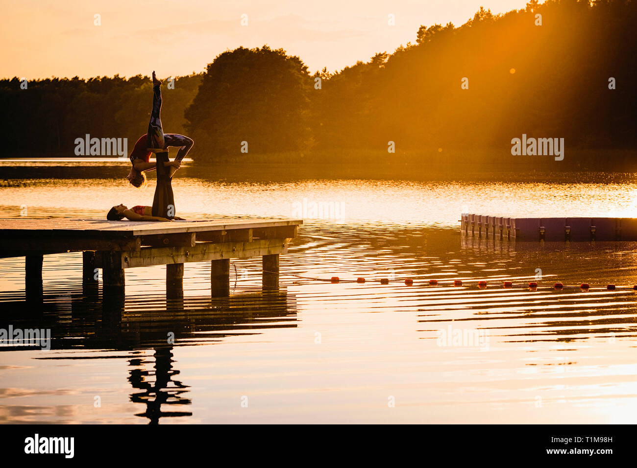 Women practicing acro yoga on lakeside dock at sunset Stock Photo