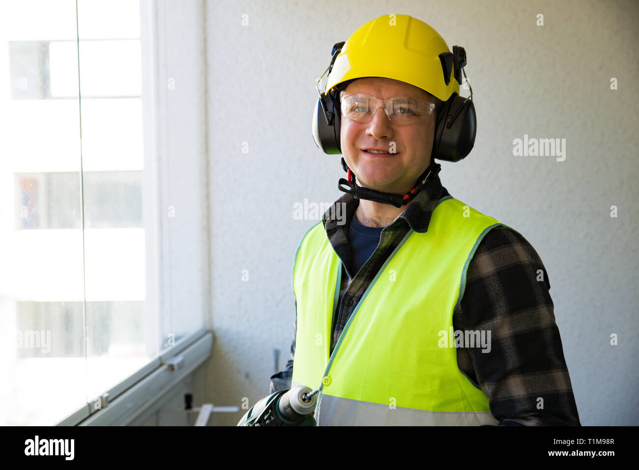 Male construction worker in hard hat with a drill and smiling at the camera. Building and renovation. Stock Photo