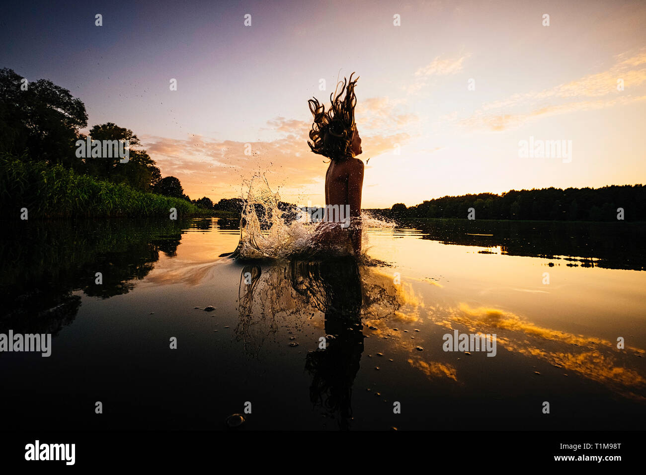 Carefree girl jumping into lake at sunset, Barnin, Mecklenburg-Vorpommern, Germany Stock Photo