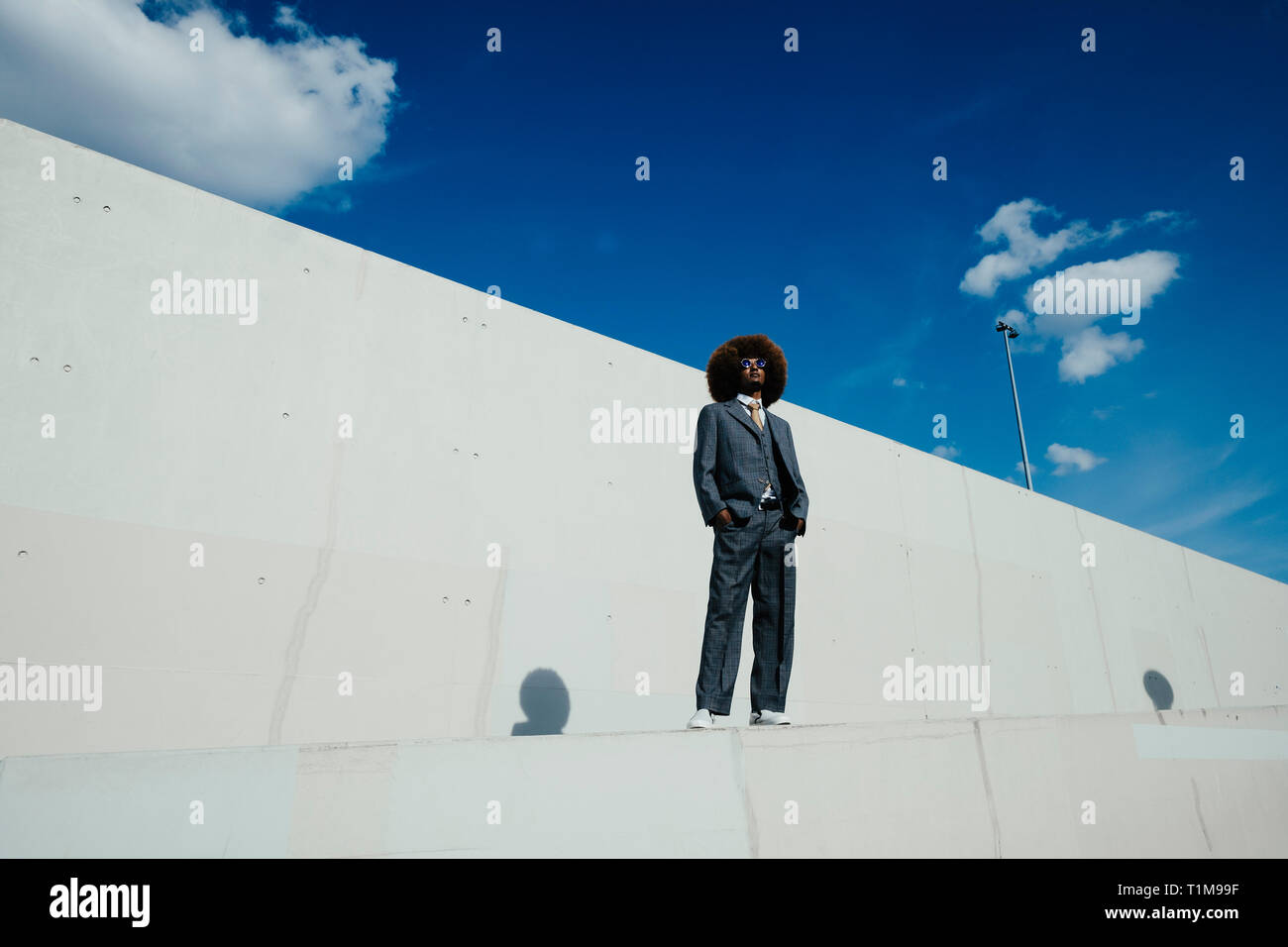 Portrait confident, cool, well-dressed young man with afro standing on urban wall Stock Photo