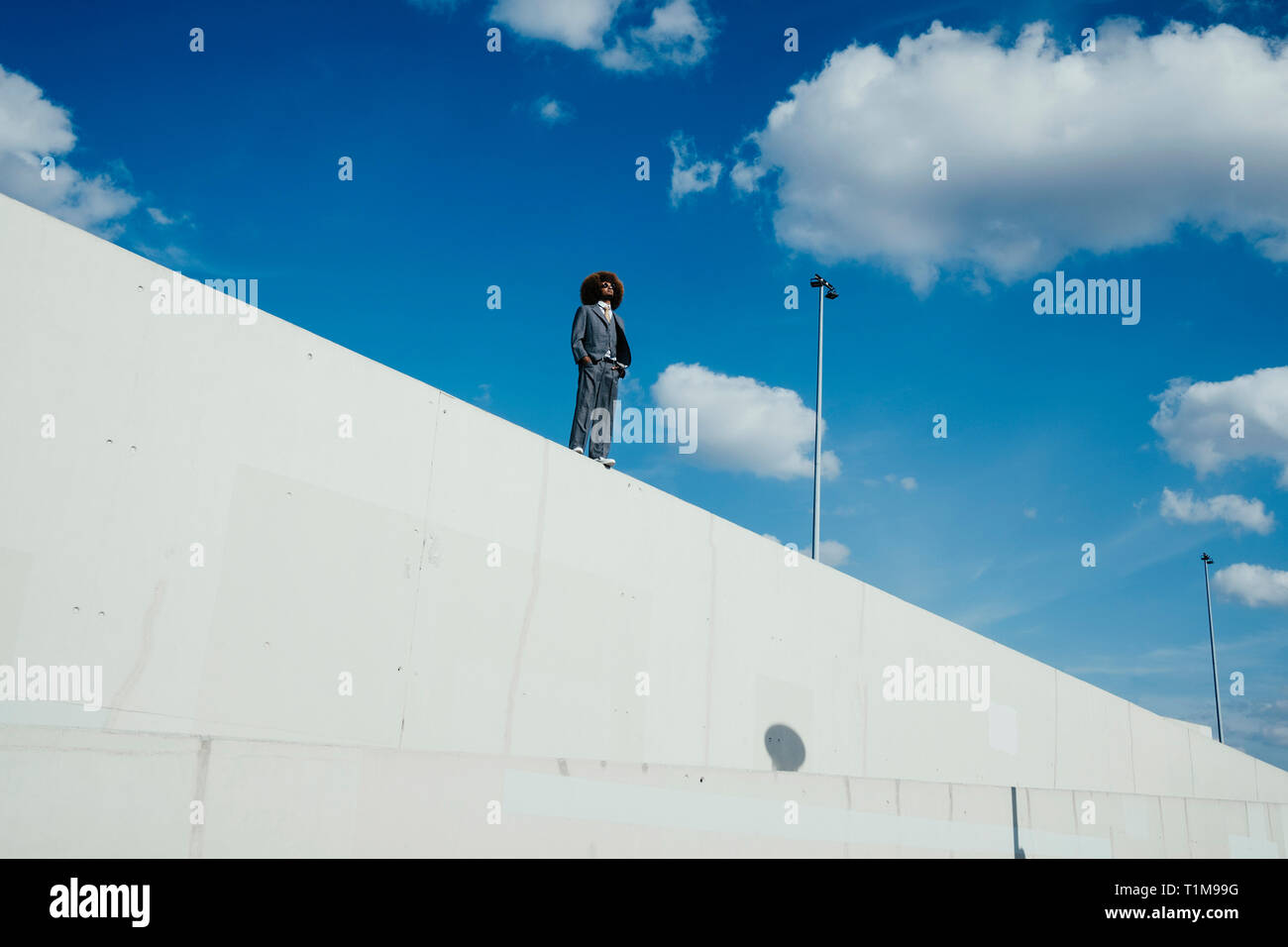 Cool, well-dressed young man with afro standing on sunny urban wall Stock Photo