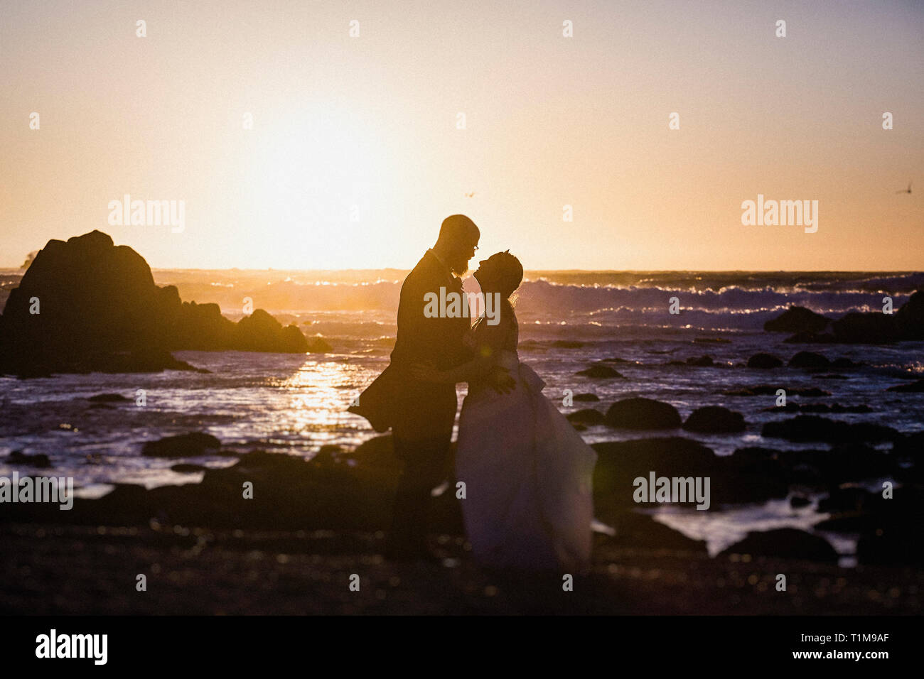 Silhouette bride and groom on tranquil sunset ocean beach, Monterey ...