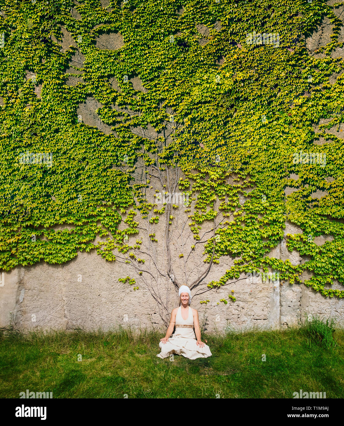 Portrait serene woman meditating at wall overgrown with ivy Stock Photo