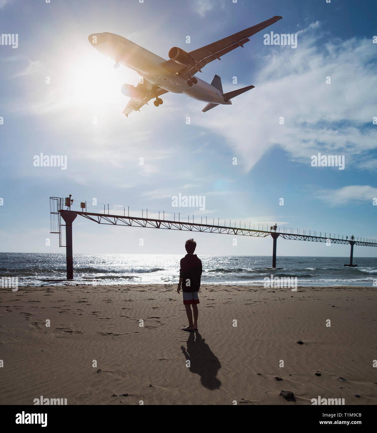 Boy looking up at airplane flying low over ocean near Lanzarote Airport, Puerto del Carmen, Spain Stock Photo