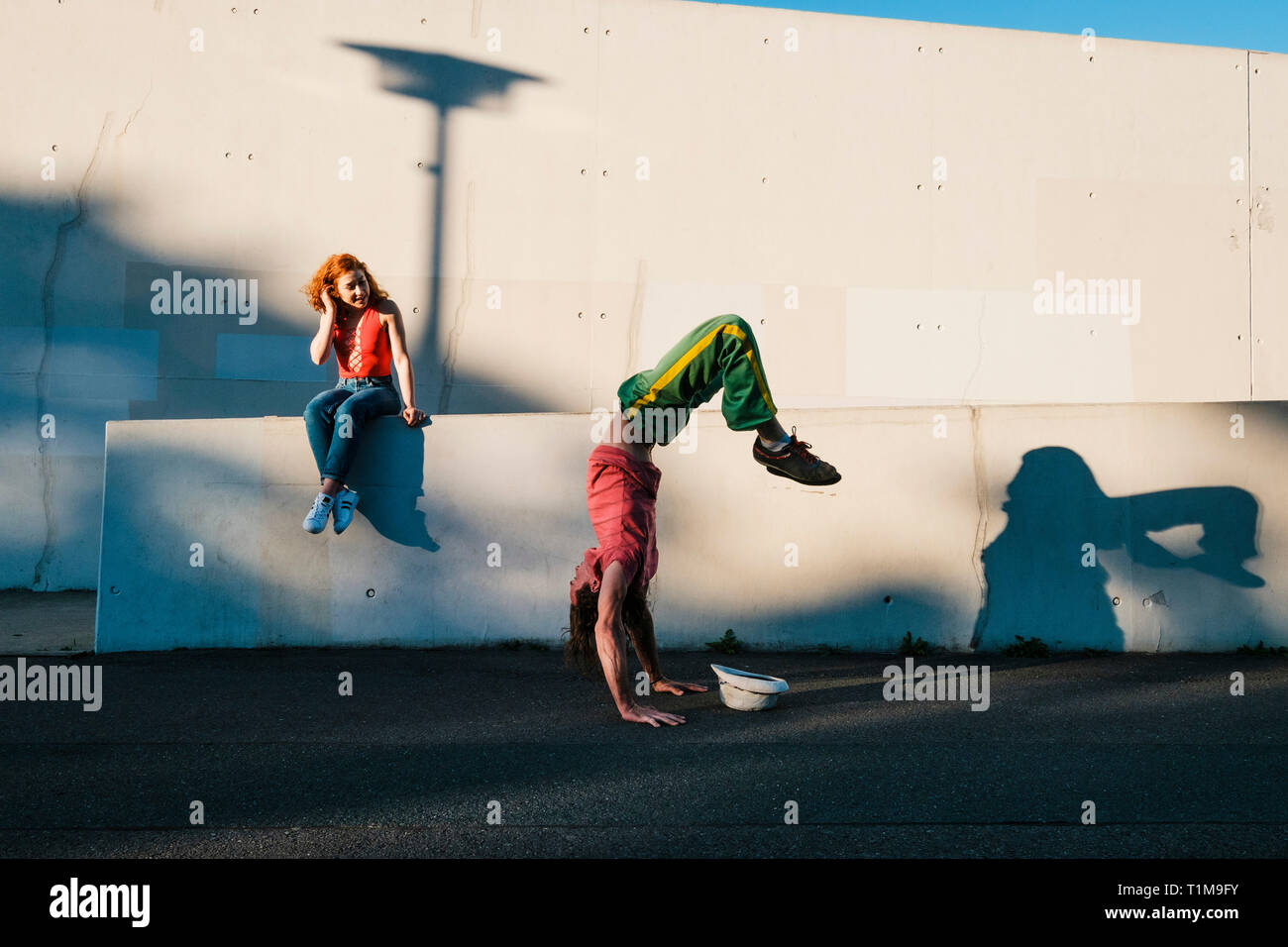Young woman watching man do handstand along urban wall Stock Photo