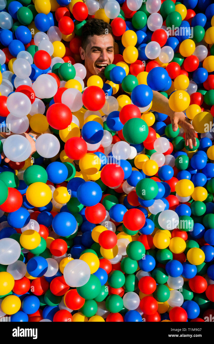 Portrait playful young man laying in multicolor ball pool Stock Photo