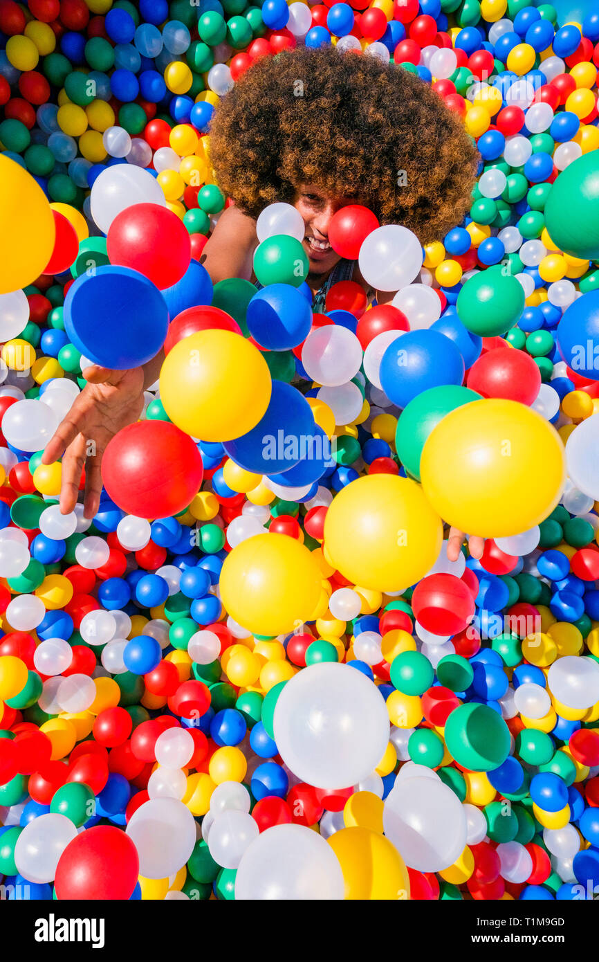 Playful young man throwing multicolor balls overhead in ball pool Stock Photo