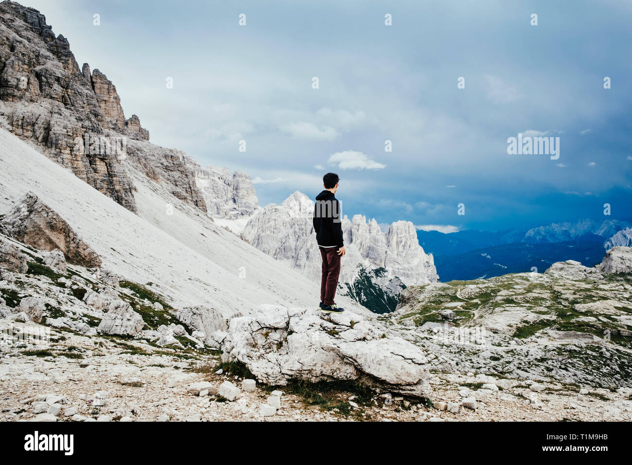 Teenage boy standing on rock overlooking rugged mountains, Drei Zinnen Nature Park, South Tyrol Stock Photo