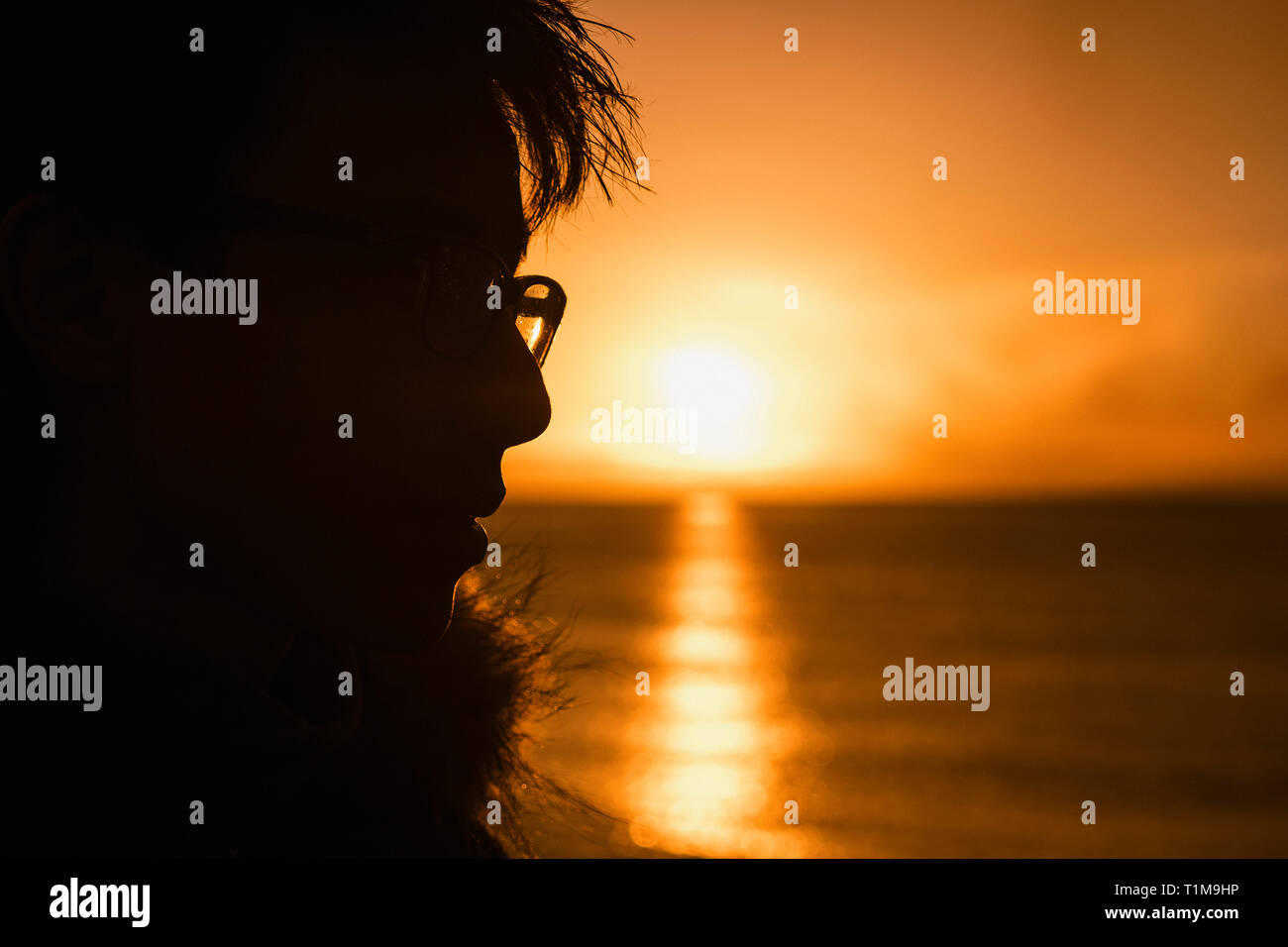 Silhouette profile teenage boy looking at sunset over ocean Stock Photo