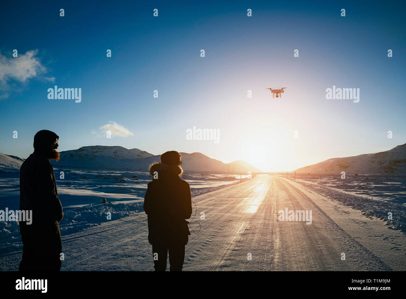 Father and son flying drone over remote, snow covered road, Reykjadalur, Iceland Stock Photo
