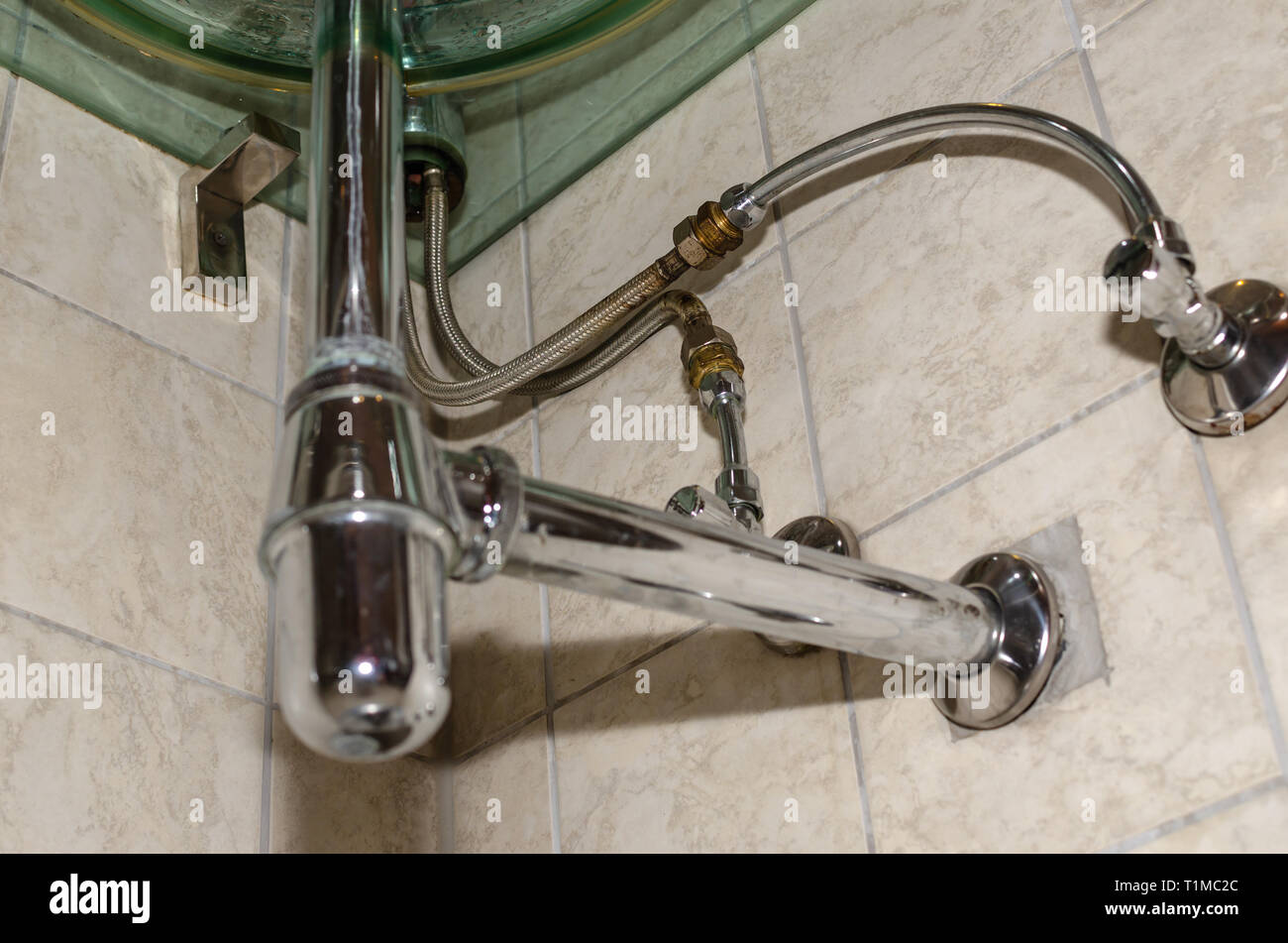 Pipe system under a glass sink in a bathroom Stock Photo