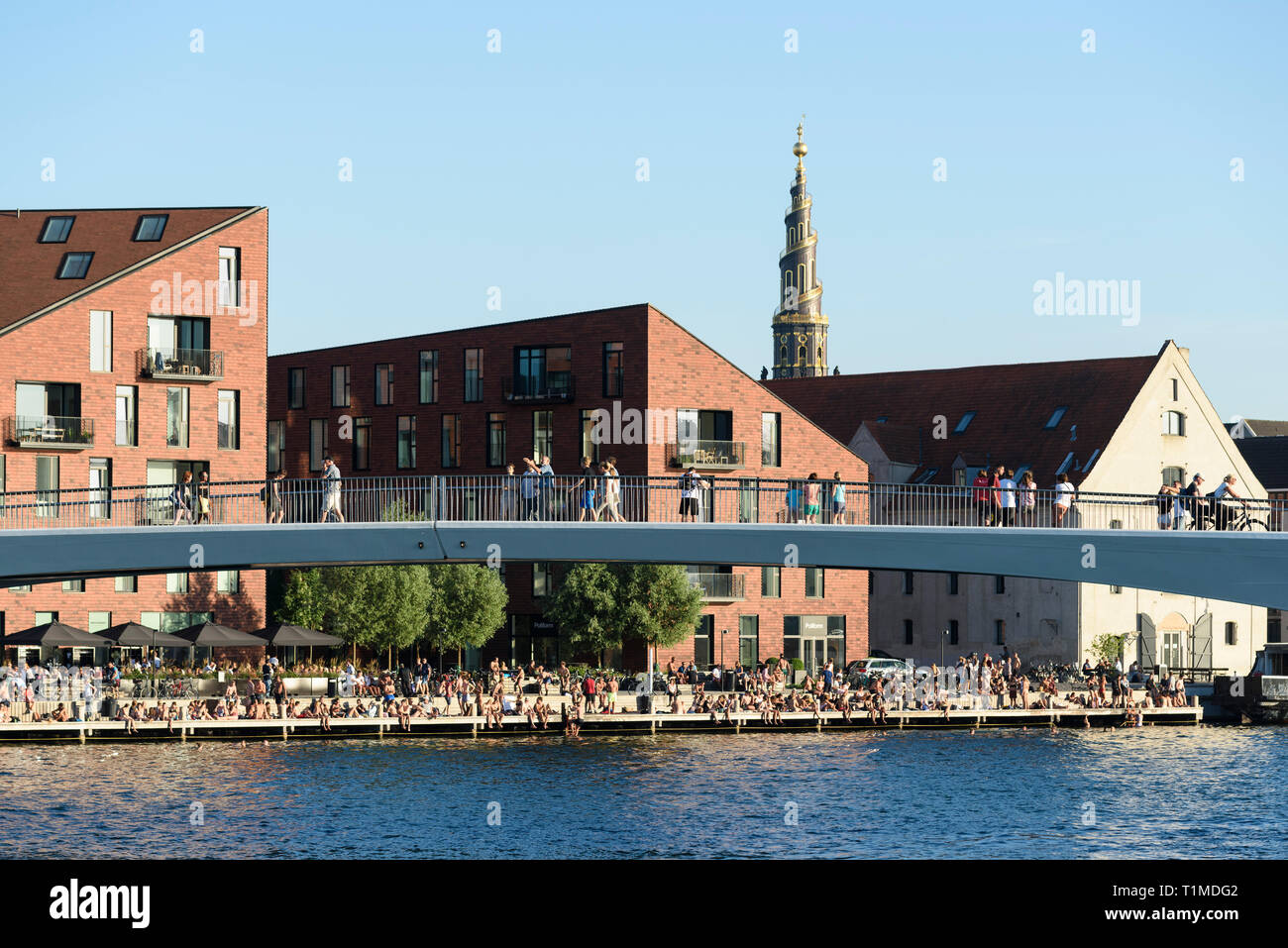 Copenhagen. Denmark. People sat on the waterfront of Christianshavn and the Inderhavnsbroen (Inner Harbour Bridge). Stock Photo