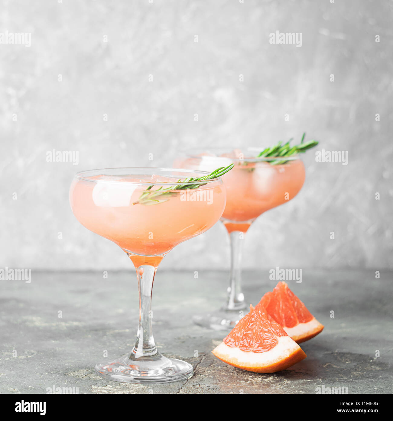 Drink grapefruit rosemary and ice in elegant glass goblets gray concrete background. Square
