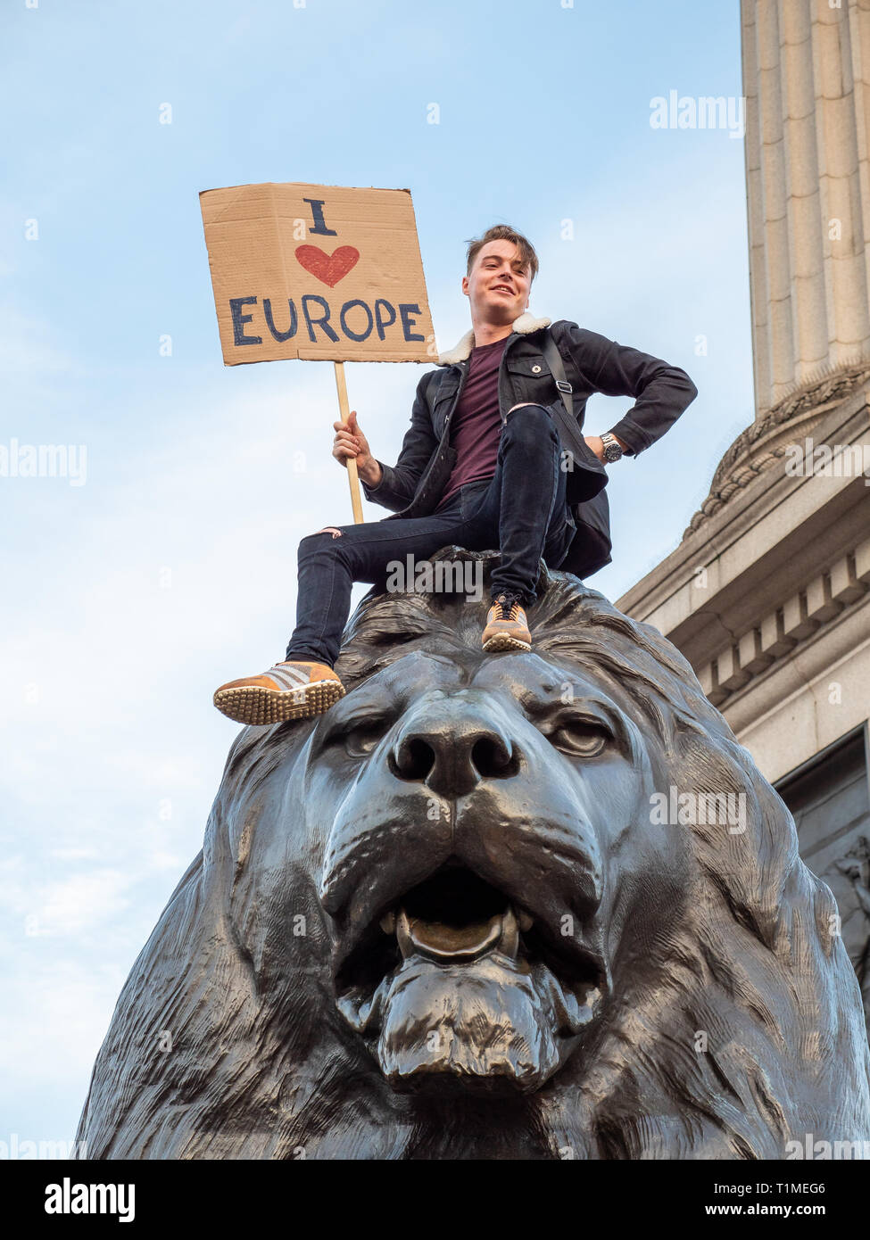 Young man sitting on one of the Trafalgar Square lions holding 'I Love Europe' sign during the People's Vote March, 23 March 2019, London, UK Stock Photo