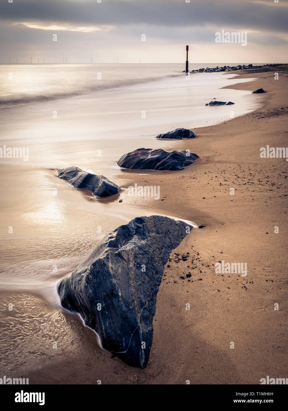 Waves and rocks on the beach as the light briefly breaks through the clouds. Stock Photo