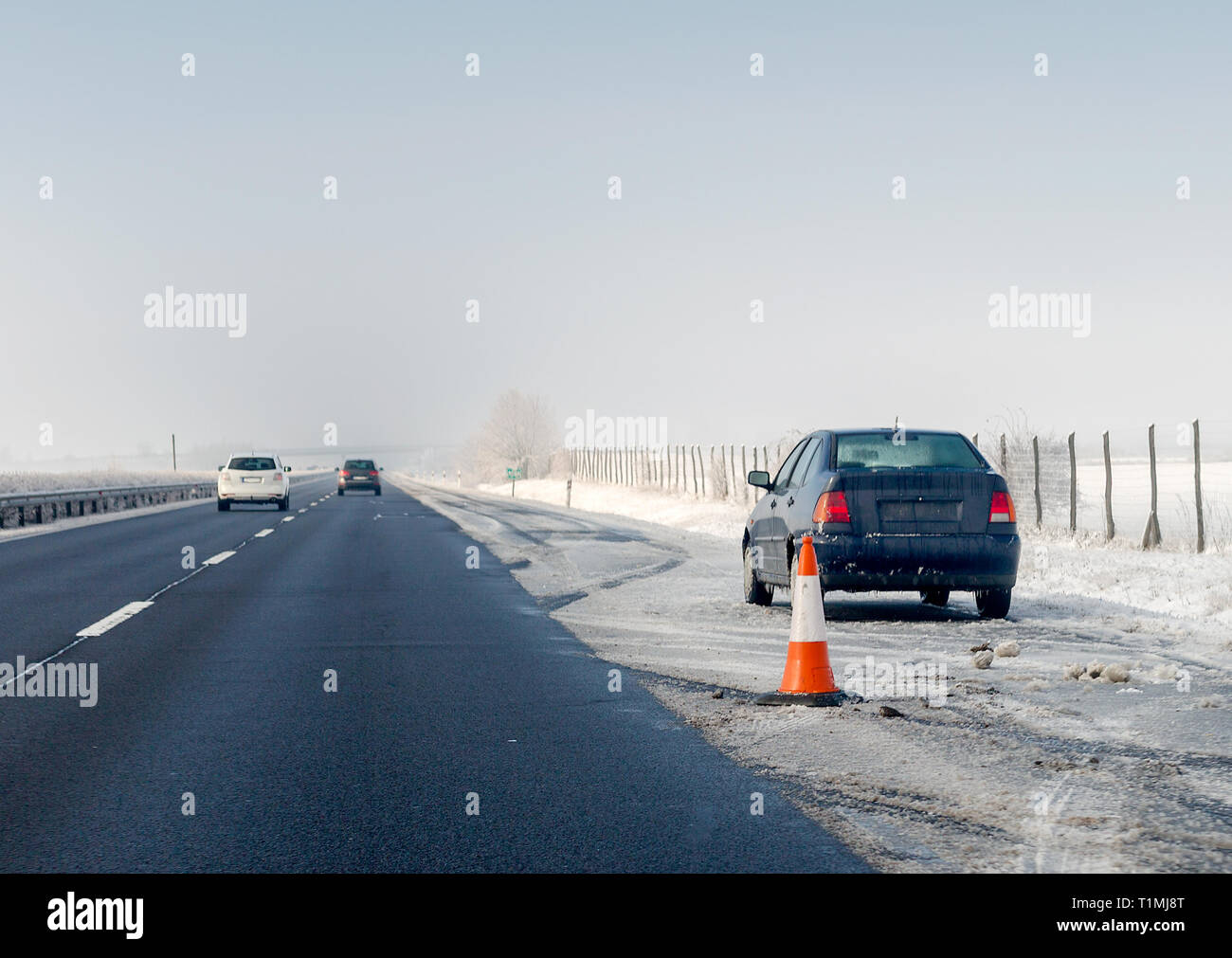 Faulty car and traffic cone on emergency stopping lane on the roadside. Problem with vehicle on winter highway. Space for text Stock Photo