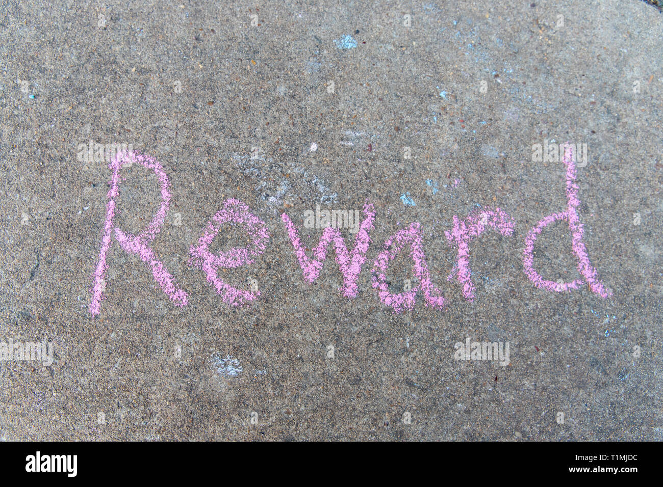 Reward written with pink sidewalk chalk on gray concrete pavement background Stock Photo