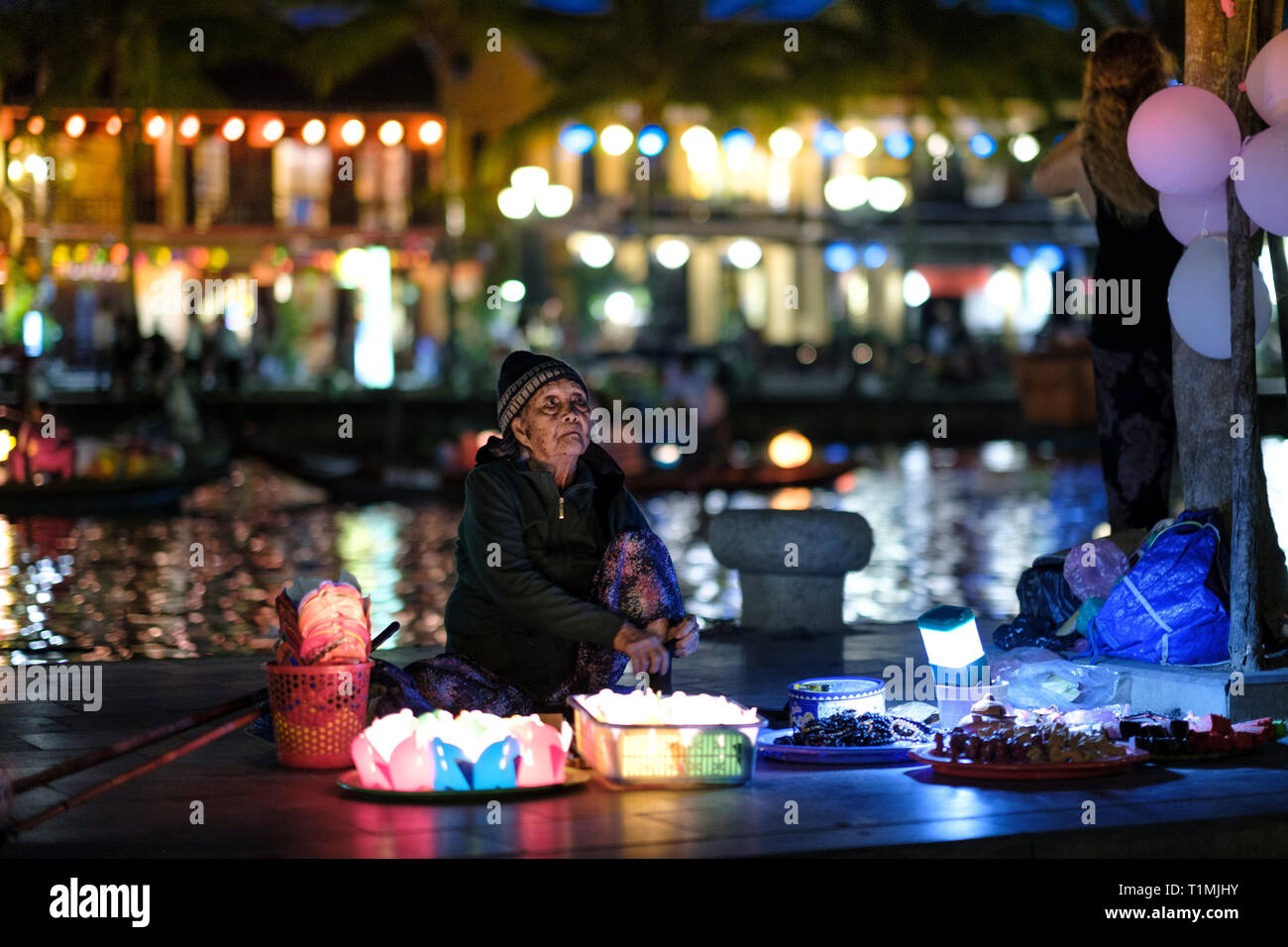 Vietnam, Hoi An. An old lady selling floating lanterns next to the Thu Bon river in the town centre. Stock Photo