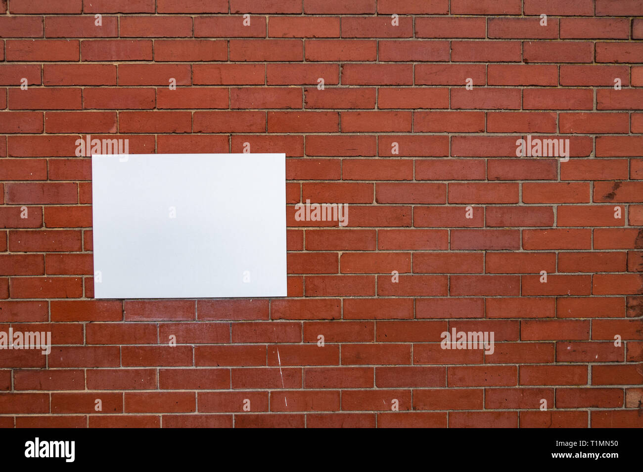 Abstract photograph of a Blank white rectangular sign panel fastened to a plain red brick wall Stock Photo