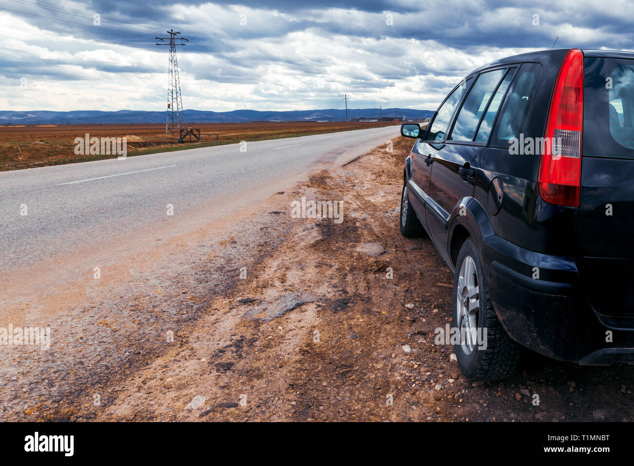 Broken car stopped by the road on stormy day, dramatic clouds on the sky Stock Photo
