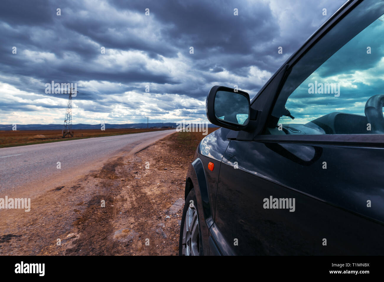 Broken car stopped by the road on stormy day, dramatic clouds on the sky Stock Photo