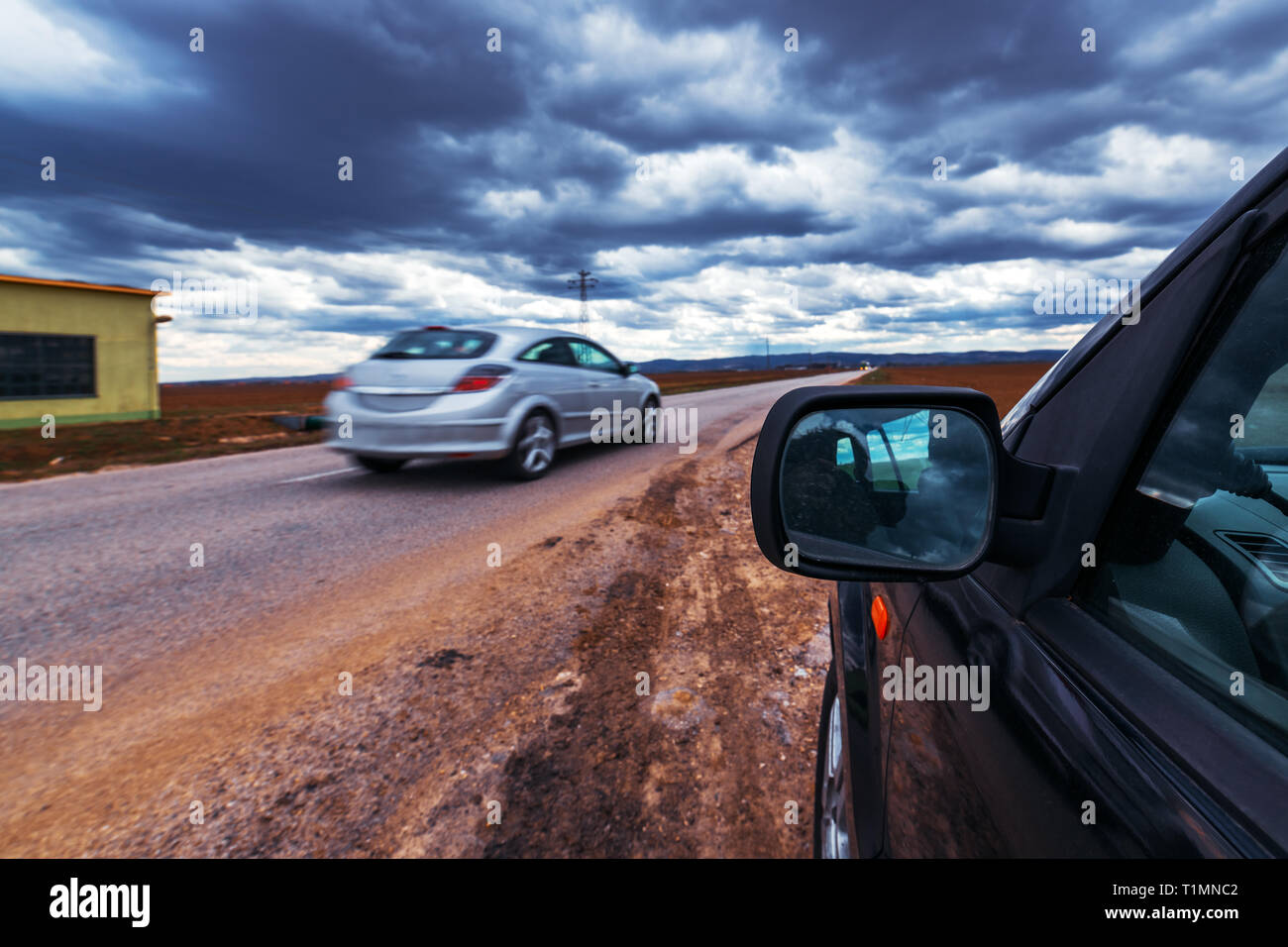 Broken car stopped by the road on stormy day, dramatic clouds on the sky Stock Photo