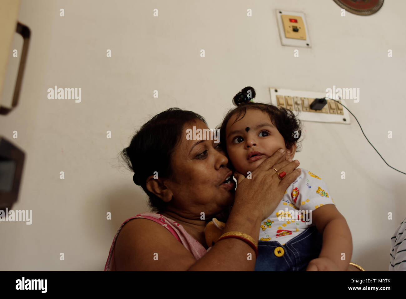 An Indian woman is showing affection to an infant girl child in a homely environment. Stock Photo