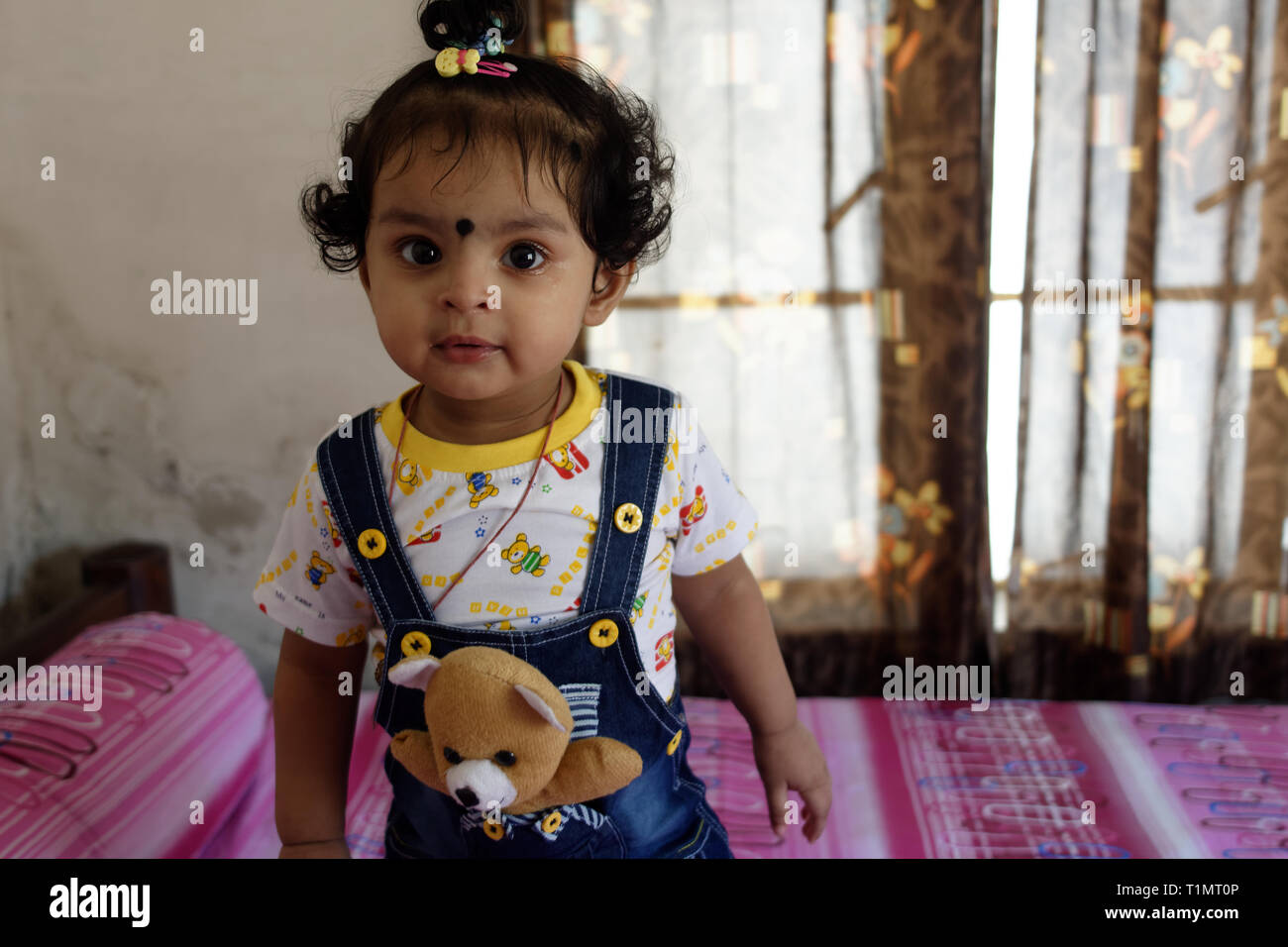 An Indian Bengali beautiful infant girl child is standing on her bed in a funny mood inside her room. Indian lifestyle Stock Photo