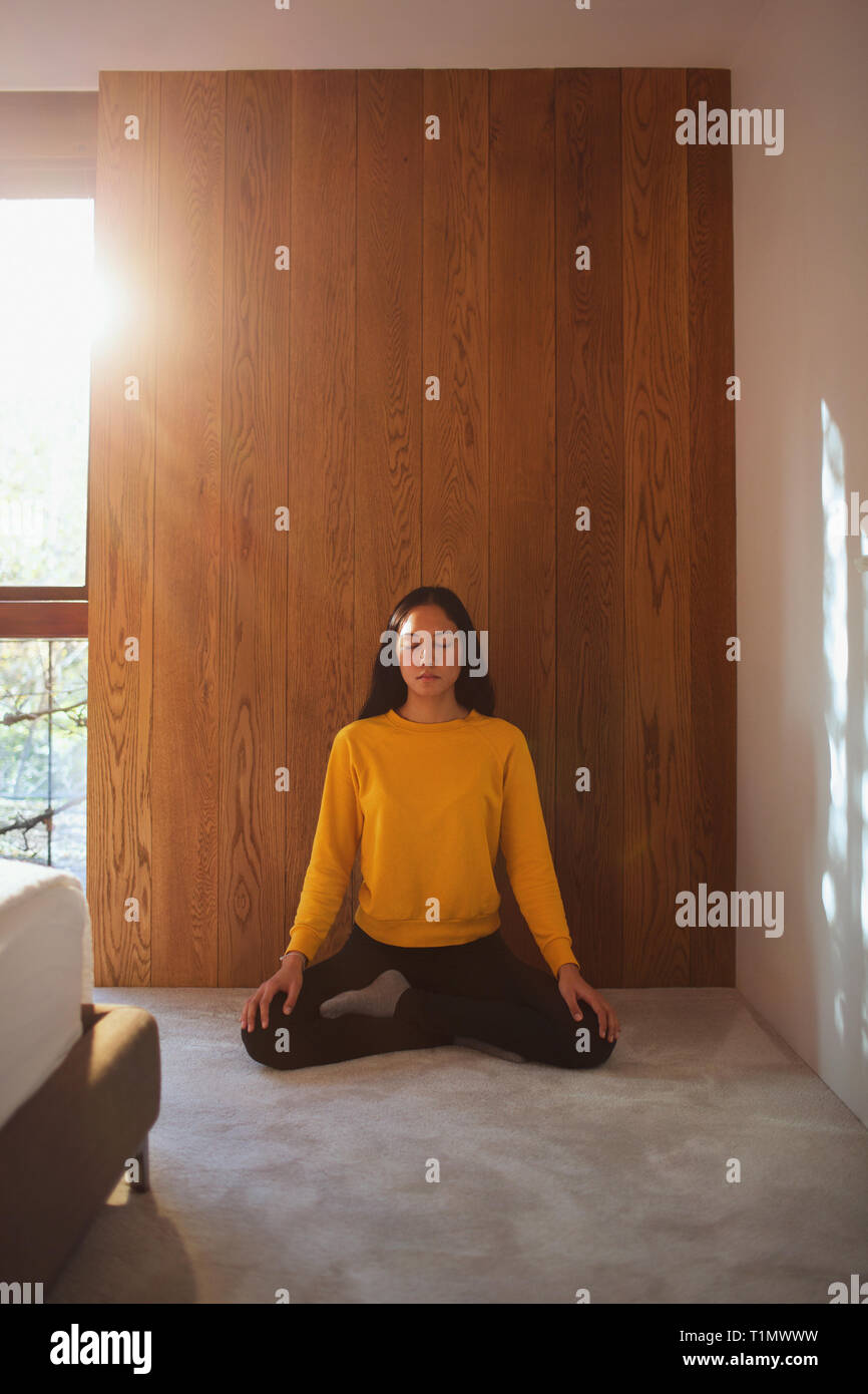 Serene young woman meditating on bedroom floor Stock Photo