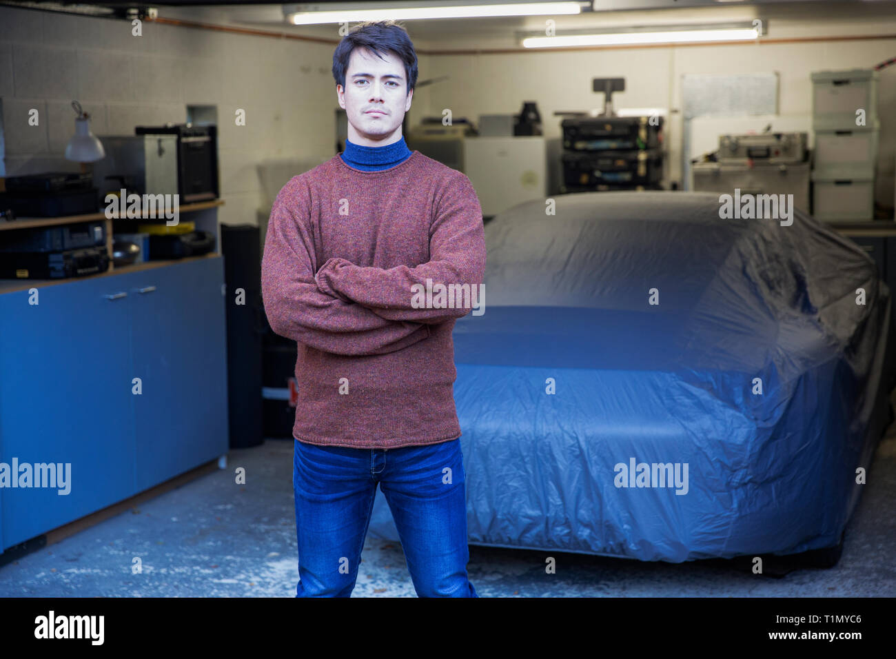 Portrait confident man standing in front of covered car in garage Stock Photo